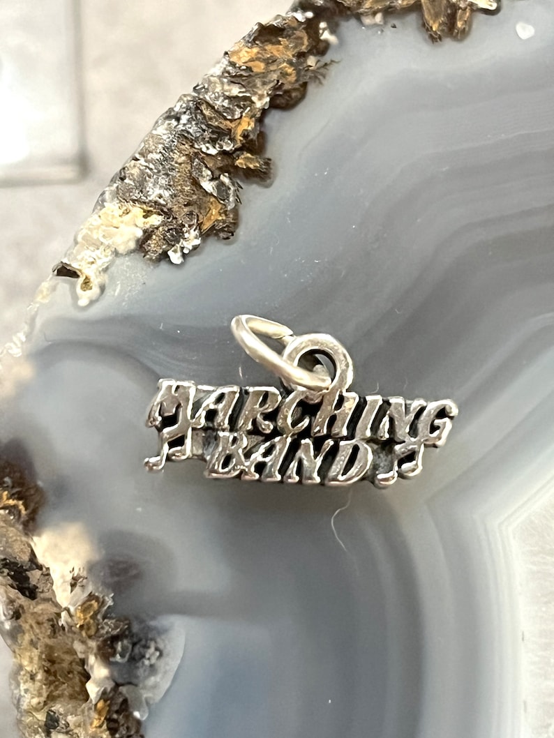 May include: Silver charm with the words "Marching Band" in a stylized font.