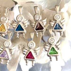 May include: A set of nine silver angel charms with different colored gemstone accents. Each charm features a small angel with wings and a gemstone in the center. The gemstones are purple, red, green, blue, and clear.