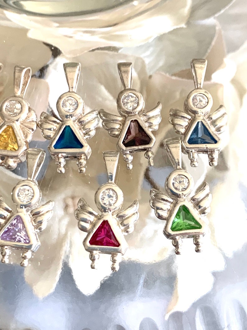 May include: A set of nine silver angel charms with different colored gemstone accents. Each charm features a small angel with wings and a gemstone in the center. The gemstones are purple, red, green, blue, and clear.