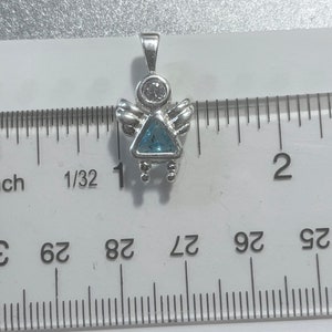 May include: Silver angel charm with a blue gemstone and a clear rhinestone. The charm is about 1 inch tall and is shown next to a ruler.