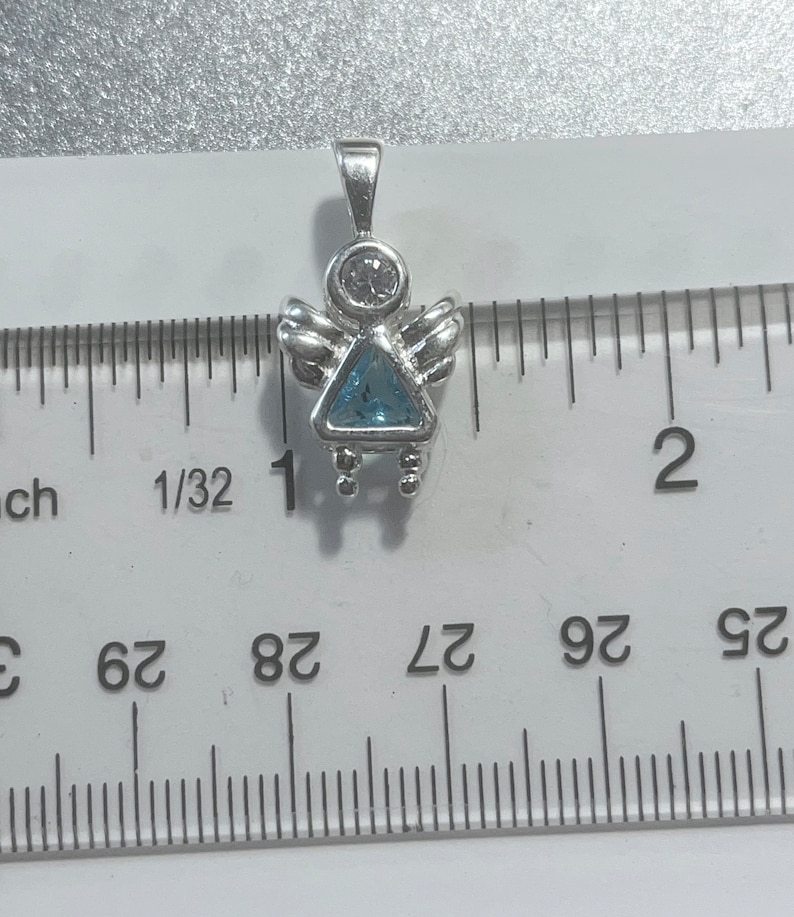 May include: Silver angel charm with a blue gemstone and a clear rhinestone. The charm is about 1 inch tall and is shown next to a ruler.