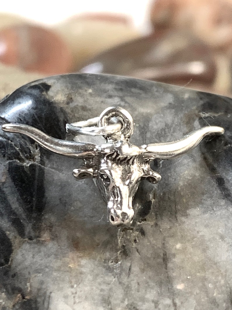 May include: Silver charm of a bull's head with horns. The charm is detailed and has a realistic look.