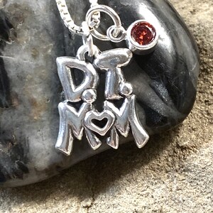 May include: Silver necklace with a charm that says "I love Mom" with two small figures holding hands and a heart. The necklace also has a small red gemstone charm.