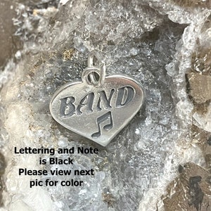 May include: Silver heart-shaped charm with the word "BAND" and a musical note. The lettering and note are black.