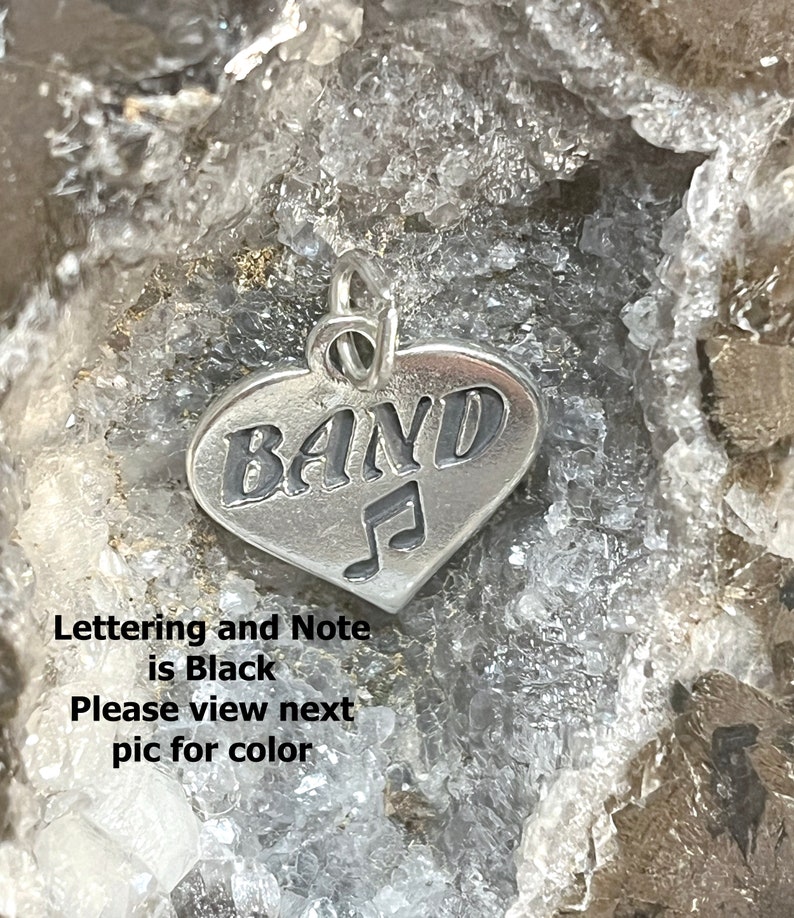 May include: Silver heart-shaped charm with the word "BAND" and a musical note. The lettering and note are black.
