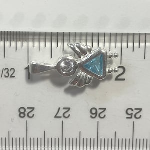 May include: Silver charm with a blue gemstone in the shape of a triangle, surrounded by wings and a small round gemstone. The charm is about 1 inch long.