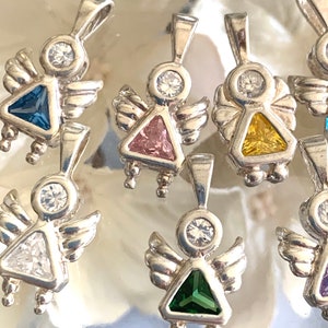 May include: A set of silver angel charms with different colored gemstone accents. The charms feature a small angel with wings and a triangular gemstone in the center. The gemstones are blue, pink, yellow, clear, green, and purple.