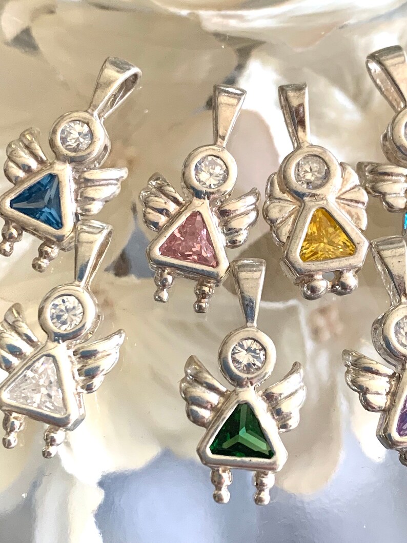 May include: A set of silver angel charms with different colored gemstone accents. The charms feature a small angel with wings and a triangular gemstone in the center. The gemstones are blue, pink, yellow, clear, green, and purple.