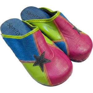 May include: A pair of Sanita clogs featuring a multi-colored patchwork design in lime green, hot pink, and blue. The shoes are accented with a black star applique on the toe box, visible stitching, and blue wooden insoles with the Sanita brand name.
