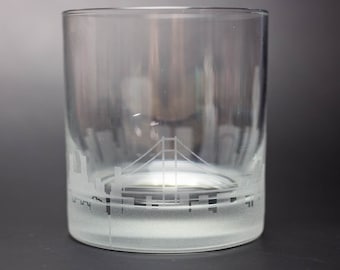 Op de afbeelding: Een helder glazen tumbler met een mat glazen stadsbeeldontwerp. Het ontwerp bevat een brug en gebouwen.