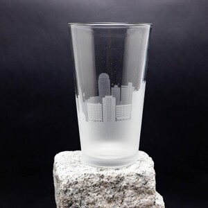 May include: A frosted glass pint glass with a white etched design of a city skyline.