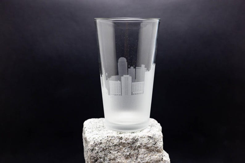 May include: A frosted glass pint glass with a white etched design of a city skyline.