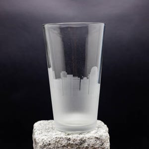 May include: A frosted glass pint glass with a white silhouette of a city skyline etched on the side.