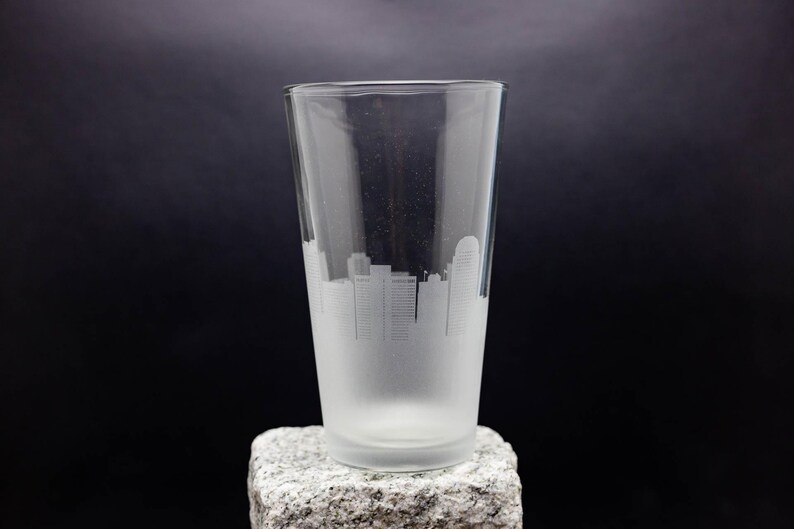 May include: A frosted glass pint glass with a white silhouette of a city skyline etched on the side.