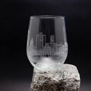 Könnte beinhalten: Ein klares Weinglas aus Glas mit einem geätzten Design einer Skyline. Das Glas steht auf einem grauen Stein.