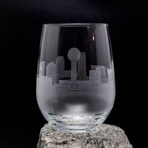 May include: A clear glass wine glass with an etched design of the Dallas skyline, including the Reunion Tower.