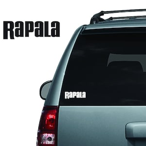 May include: A white Rapala decal is displayed on the rear window of a silver SUV. The word "Rapala" is also shown in a larger, black font on the left side of the image.