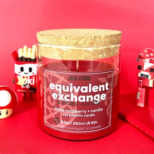 May include: A red glass candle jar with a cork lid. The label reads "GEEK STUDIO equivalent exchange scented candle black raspberry + vanilla soy paraffin candle 8.5oz | 250ml | 50h made in burlington, on canada".