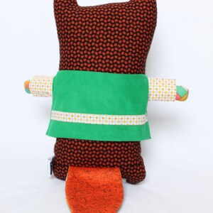 May include: A handmade stuffed fox doll with a brown body covered in small orange and black dots. It has a green sash with a white and yellow patterned trim. The fox's tail is orange with a white tip. The arms are patterned with yellow, white, and orange.