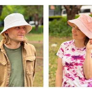May include: Two people wearing bucket hats. One person is wearing a white bucket hat and a brown jacket. The other person is wearing a pink bucket hat and a tie-dye shirt.