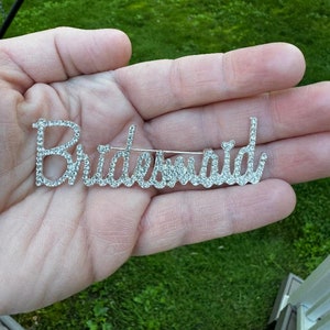May include: A silver-toned brooch with the word "Bridesmaid" spelled out in rhinestones.