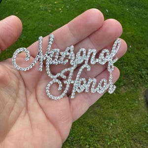 May include: A silver-toned, rhinestone-encrusted pin that reads "Maid of Honor".