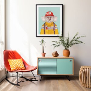 May include: A framed illustration of a koala wearing a firefighter's uniform, with a red helmet and yellow jacket. The koala is standing against a light blue background.