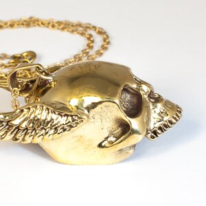 May include: A gold-tone necklace with a winged skull pendant. The skull is detailed with eye sockets and teeth.