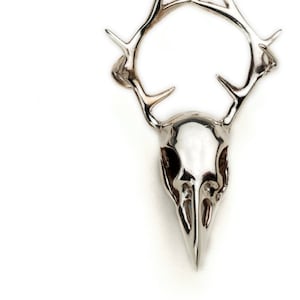 May include: Silver pendant necklace featuring a bird skull with antlers. The pendant is detailed and has a realistic look.