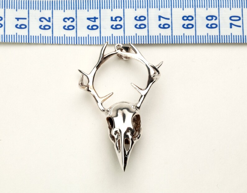 May include: Silver pendant featuring a detailed skull with antlers. The pendant is approximately 2 inches in length.