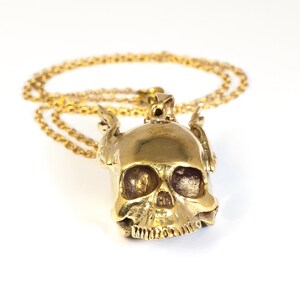 May include: A gold skull pendant with wings on a gold chain necklace.