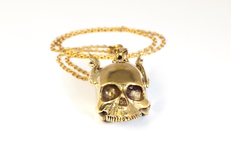 May include: A gold skull pendant with wings on a gold chain necklace.