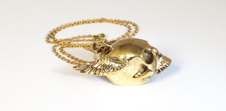 May include: A gold-tone necklace with a winged skull pendant. The skull is detailed with eye sockets and teeth.