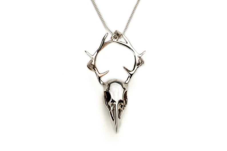May include: Silver pendant necklace featuring a bird skull with antlers. The pendant is detailed and has a realistic look.