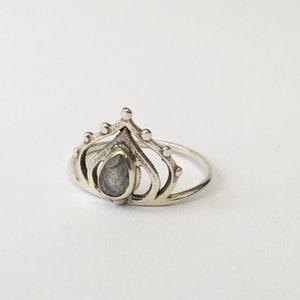 May include: A silver ring with a teardrop-shaped gemstone set in a crown design.