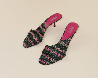 May include: A pair of black and pink floral print open-toe heels. The heels have a small stiletto heel and a pink insole with the brand name "MOSCHINO" printed on it. The shoes are set against a neutral background.
