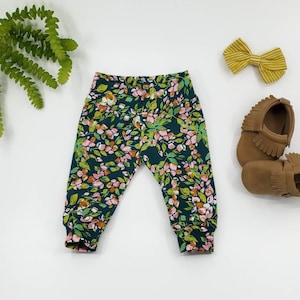 May include: A pair of dark green leggings with a floral print. The leggings have a cuffed bottom and are made of a soft, stretchy fabric.