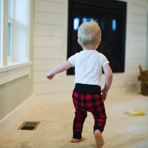 Puede incluir: Un ni&ntilde;o peque&ntilde;o con una camisa blanca y pantalones de cuadros rojos y negros camina hacia una chimenea.