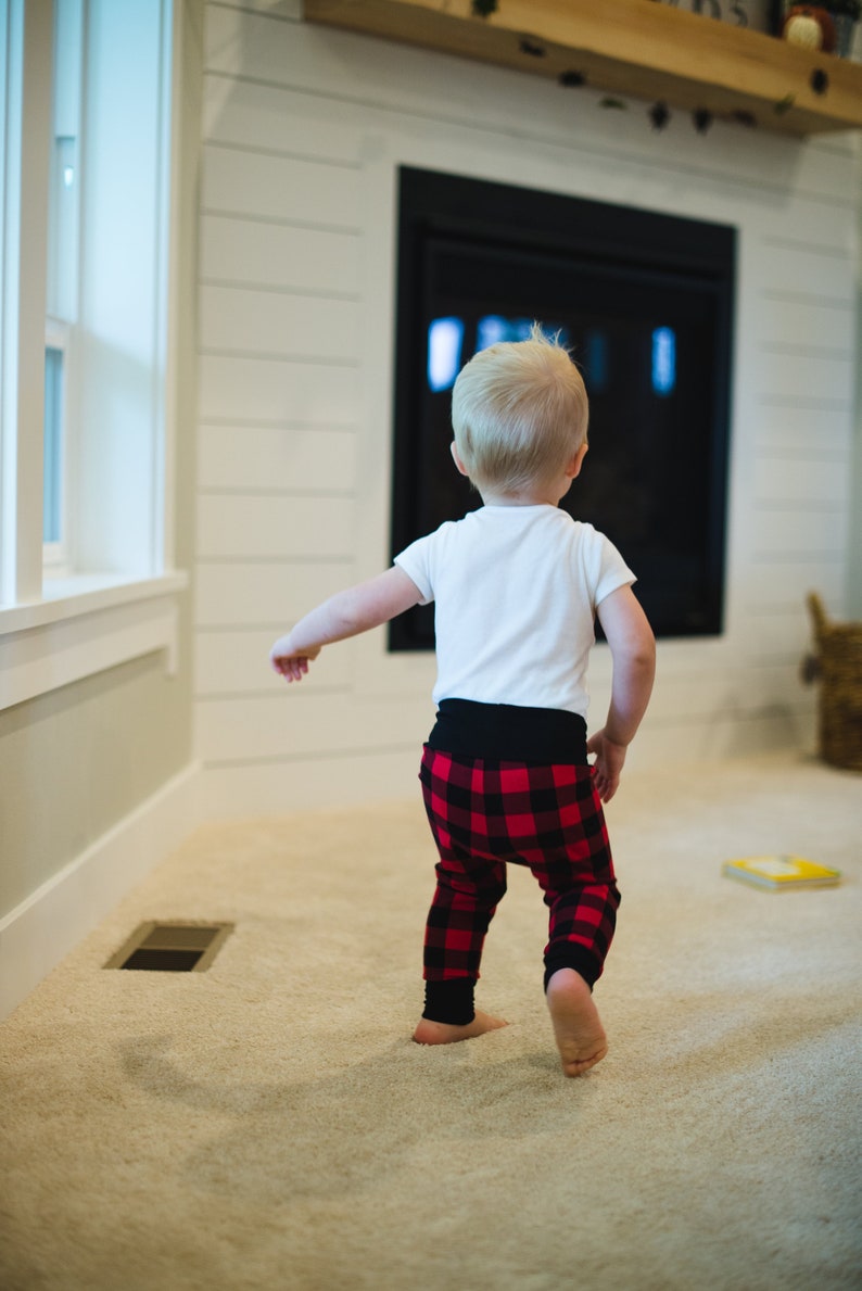 Puede incluir: Un ni&ntilde;o peque&ntilde;o con una camisa blanca y pantalones de cuadros rojos y negros camina hacia una chimenea.