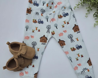 Puede incluir: Leggings blancas para bebé con estampado de animales de granja. El estampado incluye cerdos, molinos de viento, casas y tractores. Las leggings están hechas de un tejido suave y elástico.