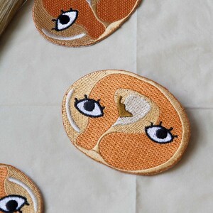 May include: Four embroidered patches shaped like slices of ham with cartoon eyes. The patches are orange and beige with white and black details.