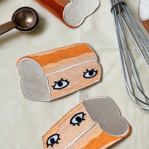 Peut inclure: Cinq patchs brodés en forme de miches de pain avec des yeux. Les patchs sont dans des tons de brun, orange et blanc.