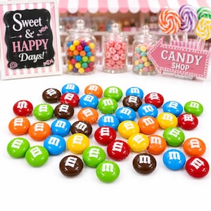 May include: A colorful candy shop scene with various candies. Scattered M&M candies in multiple colors are in the foreground. Jars filled with colorful candies, lollipops, and a sign that says "CANDY SHOP" are in the background. A sign that says "Sweet & HAPPY Days!" is also visible.