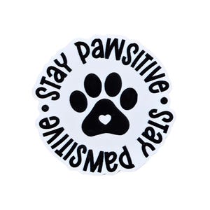 May include: A white sticker with a black paw print and a heart in the center. The words "stay pawsitive" are written in a circular pattern around the paw print in black.