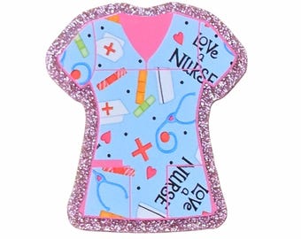 May include: A light blue scrub top shaped pin with a pink glitter border. The pattern features medical icons like stethoscopes, nurse caps, and bandages, along with red hearts and the text Love a Nurse printed in black lettering throughout.