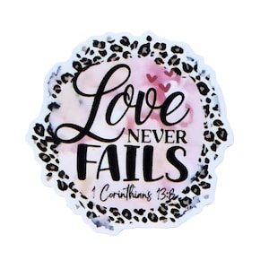 May include: A sticker with the words "Love Never Fails" in black script and block letters. The sticker has a watercolor background with pink and purple hues, and a leopard print border. The Bible verse 1 Corinthians 13:8 is also included.