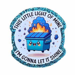 May include: A circular sticker with a teal glitter border featuring a cartoon blue dumpster on fire. The dumpster has a smiling face with pink cheeks. The text reads THIS LITTLE LIGHT OF MINE I'M GONNA LET IT SHINE in black capital letters.