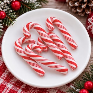 May include: A collection of five red and white striped candy canes arranged on a plain white circular plate. The candy canes feature a classic hooked shape with diagonal red stripes against a white background, creating a festive appearance.