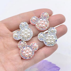 May include: Four pink and white mouse-shaped embellishments with pearl and iridescent rhinestones.