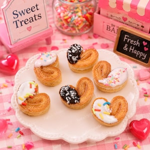 May include: A collection of heart-shaped pastries with white icing and colorful sprinkles, some with chocolate topping, arranged on a white plate. The image includes a sign that says "Sweet Treats" and a sign that says "Fresh & Happy".